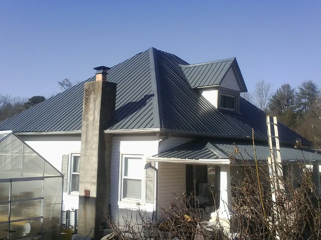 Dark blue standing seam metal roof on a white farmhouse with dormer — Slate & Tile Roof Repair by Roofing Brothers in East Earl