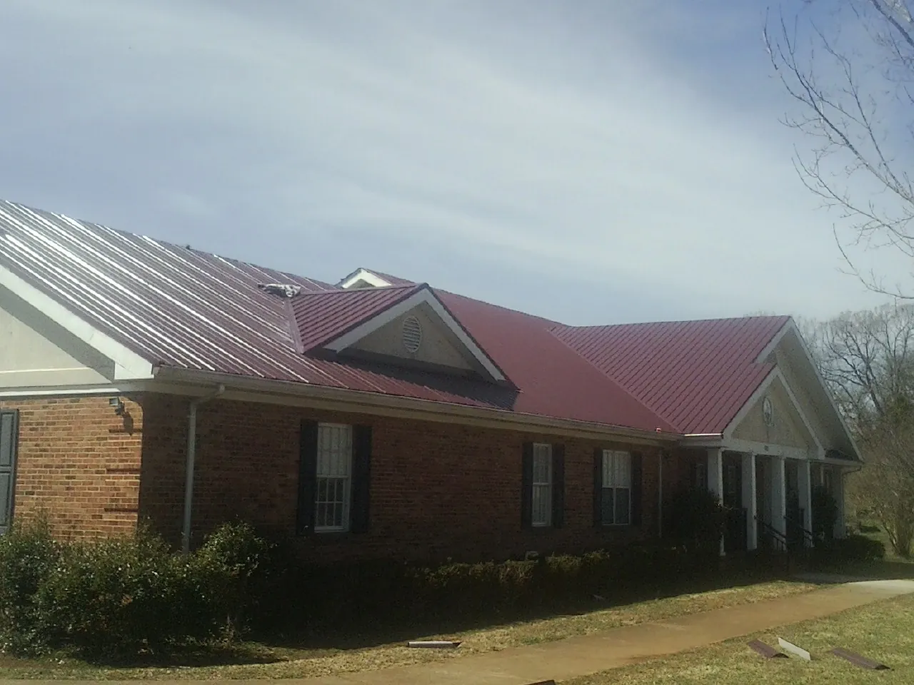 Red metal roof with gabled entries on a long brick building, from a Hail Damage Roof Repair job in East Earl