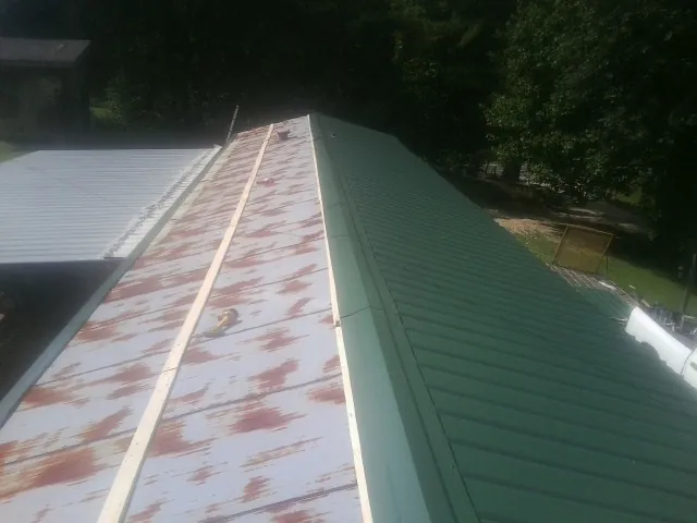 Old rusted panels beside newly installed green metal roofing — Wind Damage Roof Repair by Roofing Brothers in East Earl