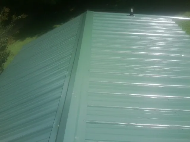 New green metal panels meeting at the ridge of a roof — Flat Roof Repair work by our crew in East Earl