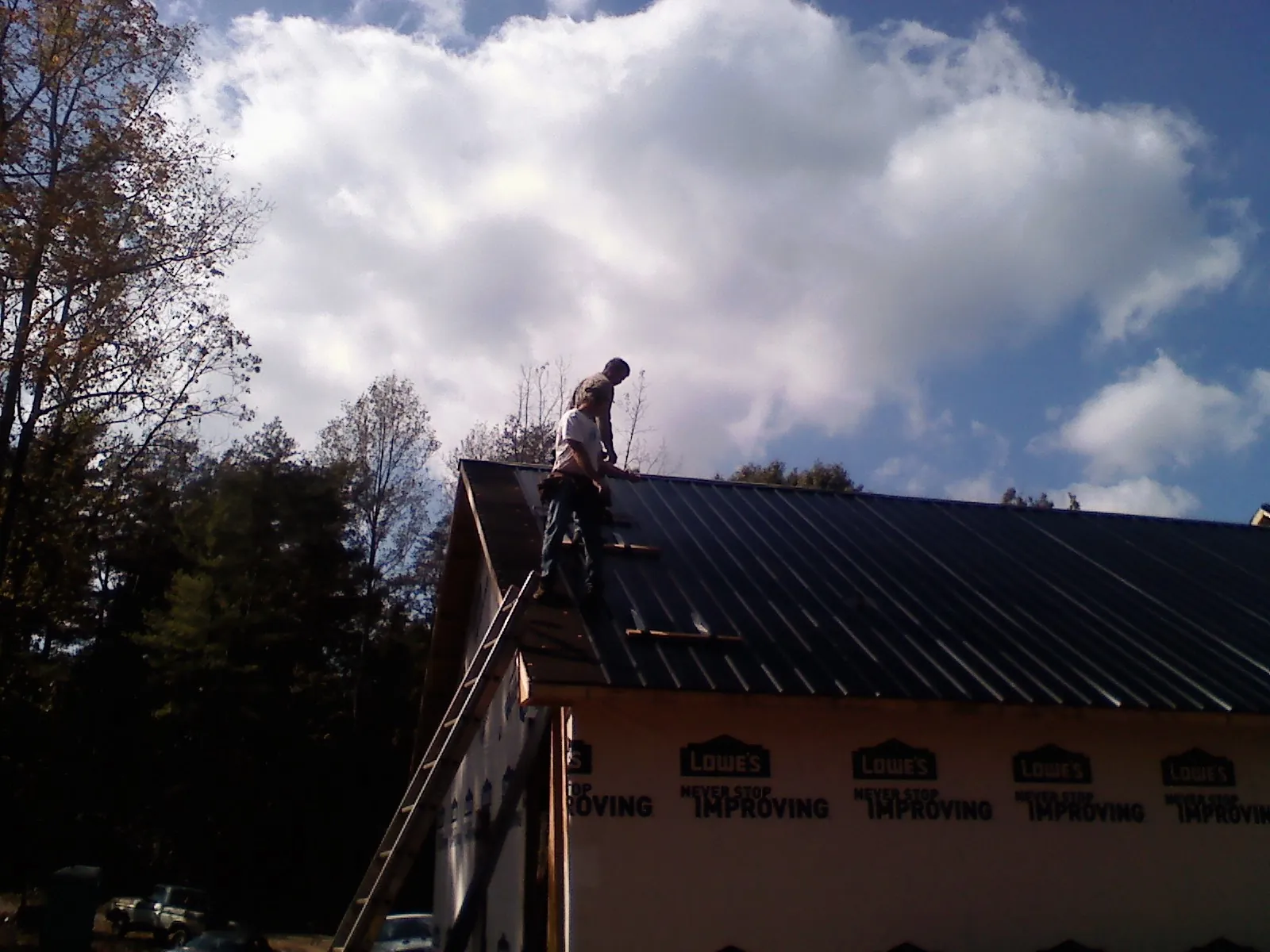 Roofer fastening dark metal panels high against a cloudy sky, from a Roof Inspection job in East Earl