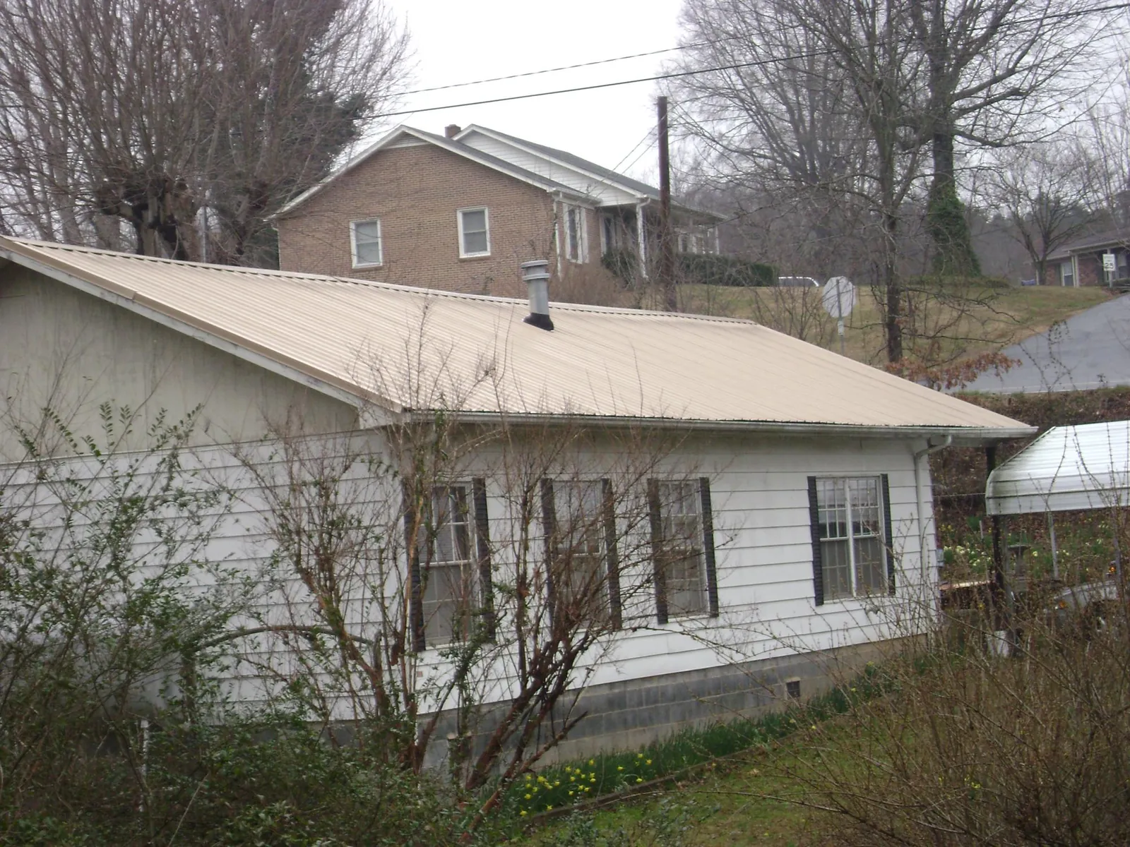 Tan metal roof on a white sided house set into a hillside — Commercial Roofing by Roofing Brothers in East Earl