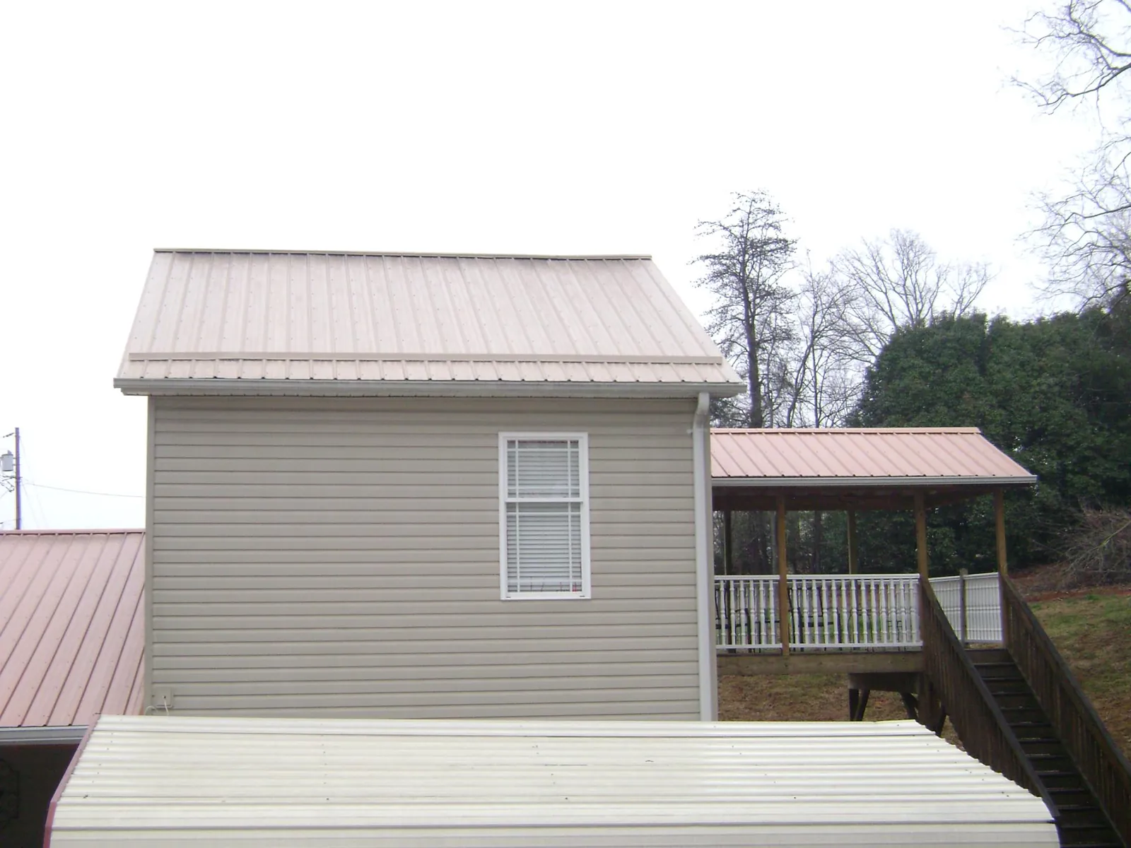 Tan metal roofs on a two story addition and attached porch, from a Roof Replacement job in East Earl